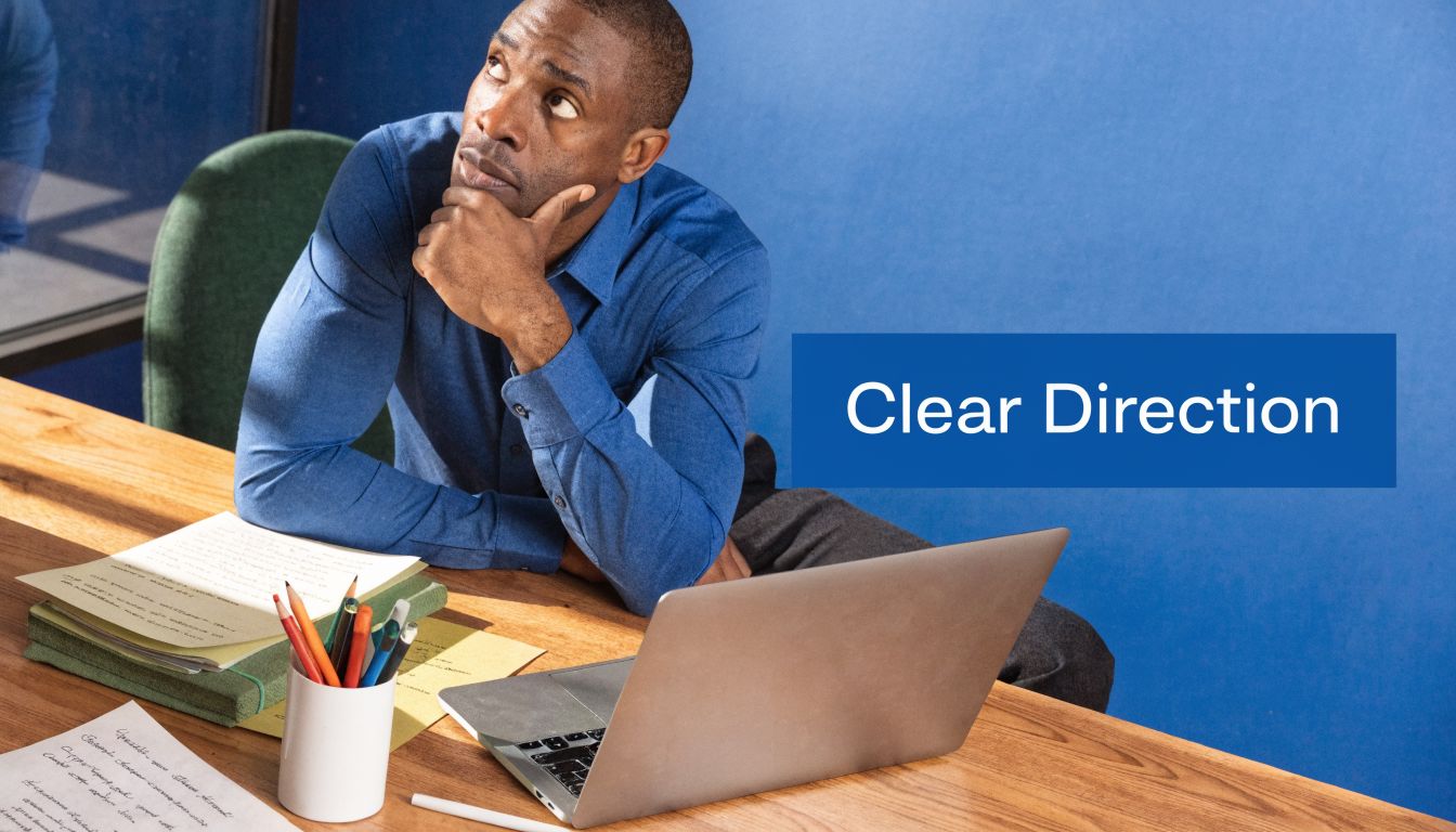 A professional man sitting at a desk thinking while looking at a laptop and documents.